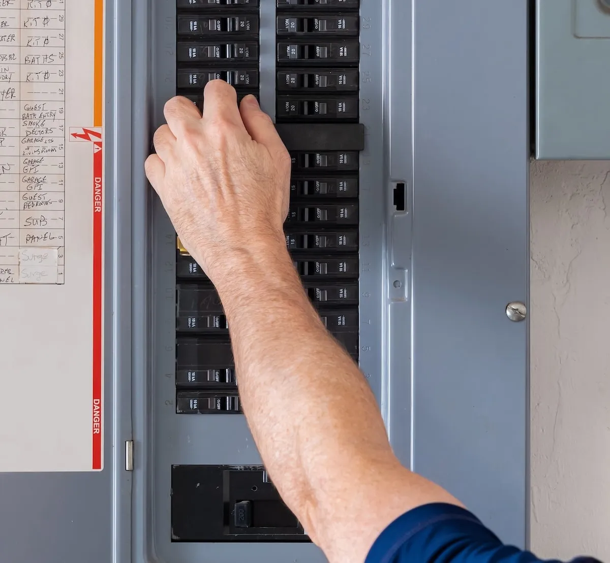 Person's hand turning off a circuit breaker switch in an electrical panel.
